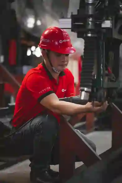 Man in red helmet adjusts machine in industrial factory setting.